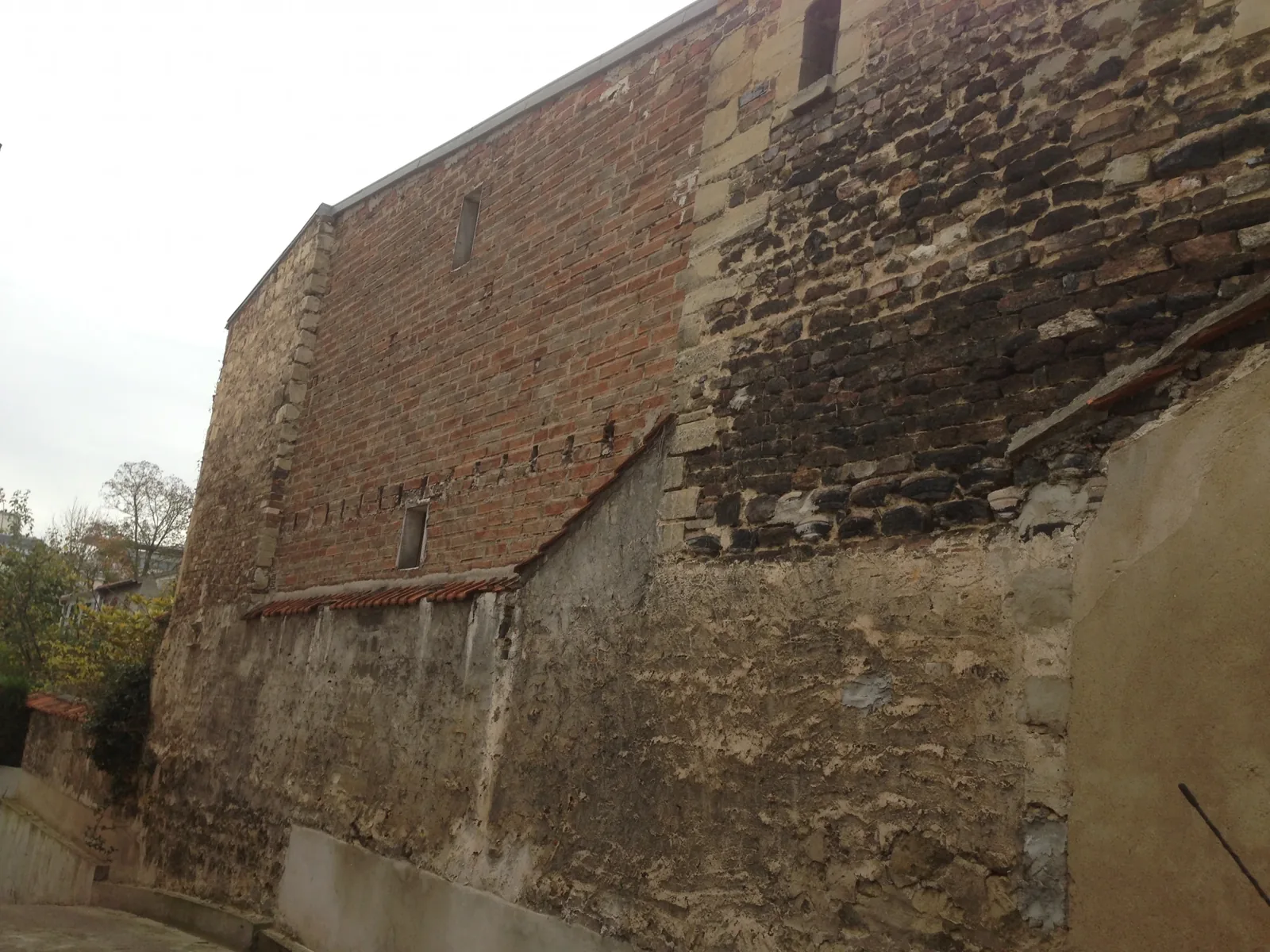 Muret ancien à Paris 9ème avec enduit ciment décollé par plaques et moellons calcaires apparents avant travaux Muret ancien à Paris 9ème avec enduit ciment décollé par plaques et moellons calcaires apparents avant travaux