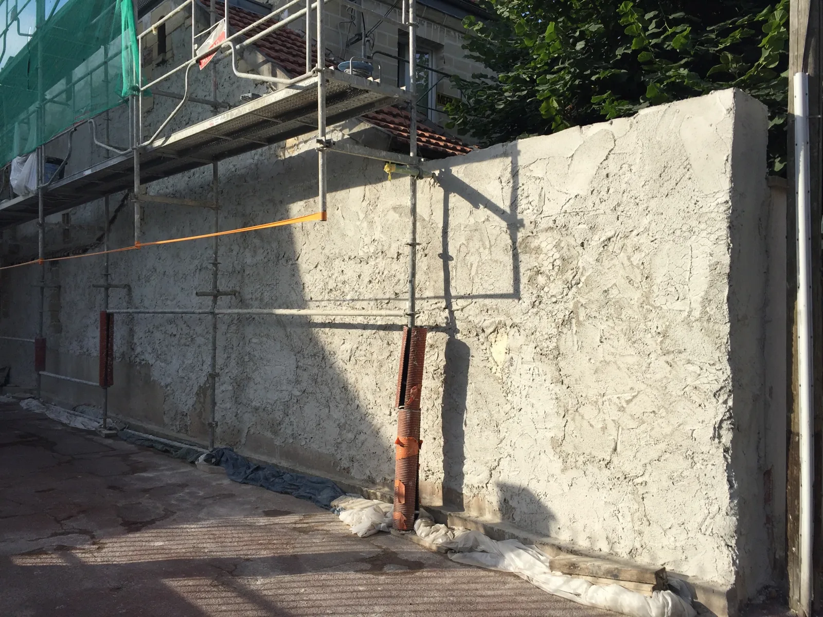 Application de l'enduit à la chaux hydraulique sur le muret à Paris 9ème pendant le chantier, avec échafaudage